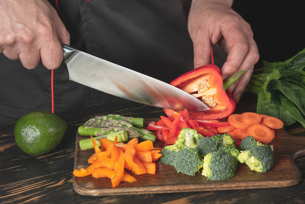 Close view of male chef slicing red bell pepper on wooden chopping board - Foto, Bild