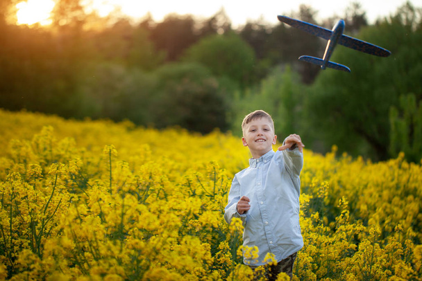 Junge wirft Spielzeugflugzeug an einem Sommertag bei Sonnenuntergang. - Foto, Bild