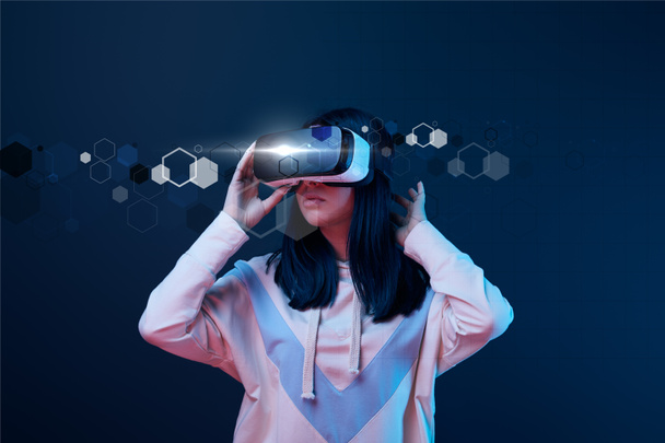 young woman in virtual reality headset among cyber illustration on dark background - Photo, Image