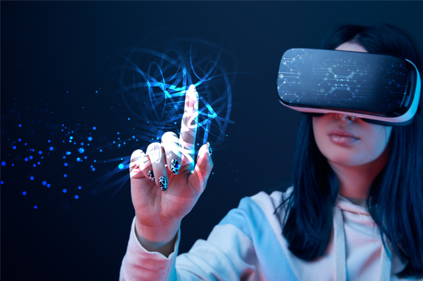 szelektív középpontjában a fiatal nő a virtuális valóság headset mutatott ujjal izzó Cyber illusztráció sötét háttér - Fotó, kép