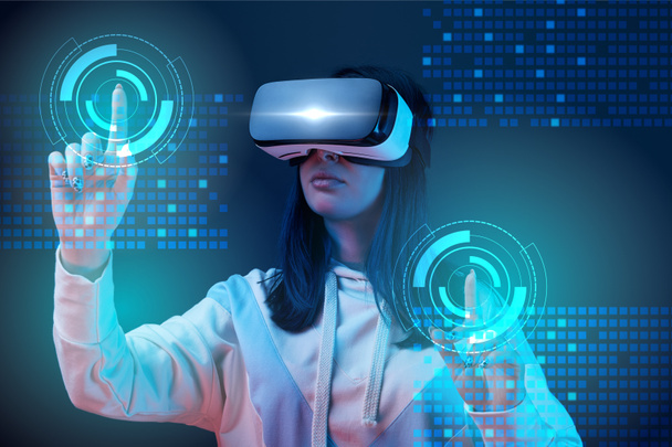 young woman in vr headset pointing with fingers at glowing cyber illustration on dark background - Photo, Image