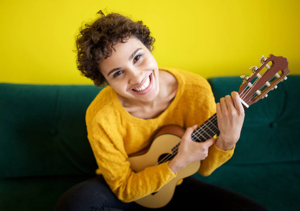 Retrato de feliz joven afroamericana sentada con instrumento de guitarra
 - Foto, imagen