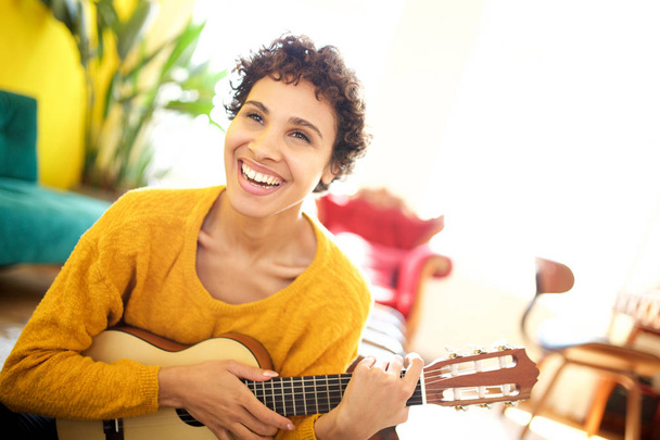 Retrato de una joven afroamericana sonriendo con la guitarra en casa
 - Foto, imagen