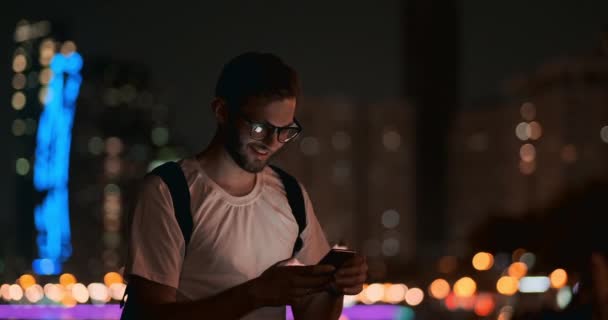 Geceleri gözlüklü genç bir adam akıllı telefonun ekranına bakıyor. - Video, Çekim