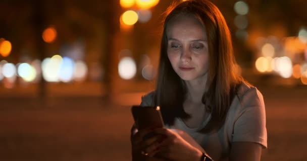 夜の街の若い女の子はスマートフォンでテキストメッセージを書きます - 映像、動画