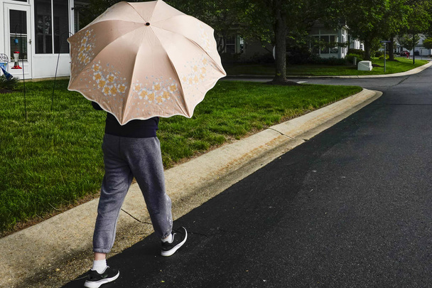 ソロモンズ島、メリーランド州、アメリカ合衆国 女性が太陽に対して傘を持って通りを歩く. - 写真・画像