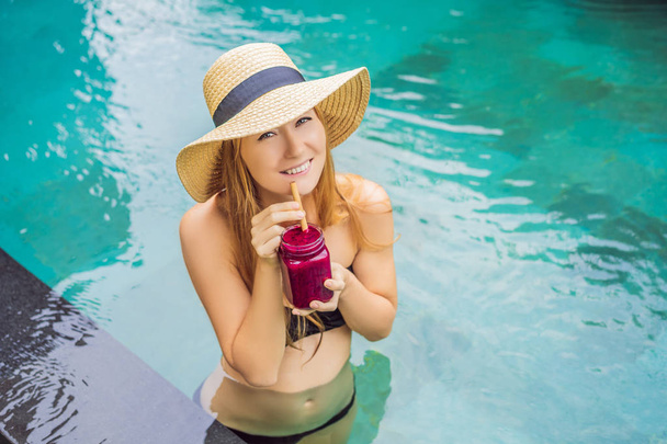 Young woman drinking Dragon fruit smoothies on the background of the pool. Fruit smoothie - healthy eating concept. Close up of detox smoothie with Dragon fruit - Foto, imagen