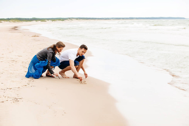 Молодая пара на пляже рисует в песке
. - Фото, изображение