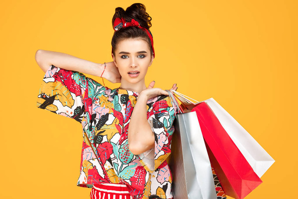 Joven mujer caucásica feliz en ropa colorida casual sosteniendo bolsas y compras sobre fondo naranja. Concepto de compras y ventas
. - Foto, Imagen