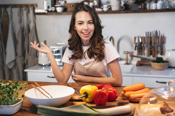 Beautiful young woman wearing apron cooking vegetables - Foto, imagen