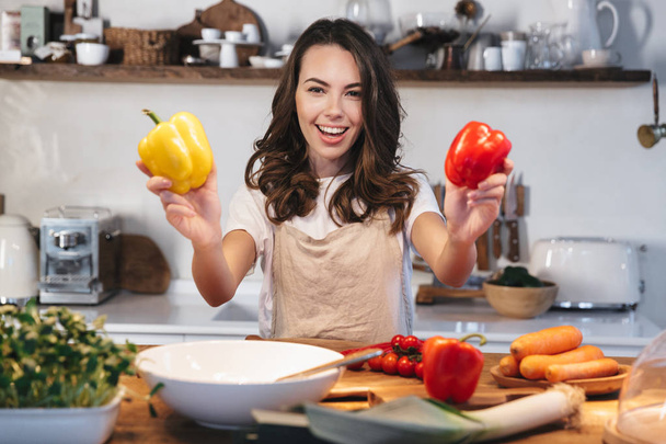 Beautiful young woman wearing apron cooking vegetables - Foto, afbeelding