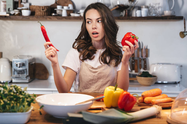 Beautiful young woman wearing apron cooking vegetables - Foto, Bild