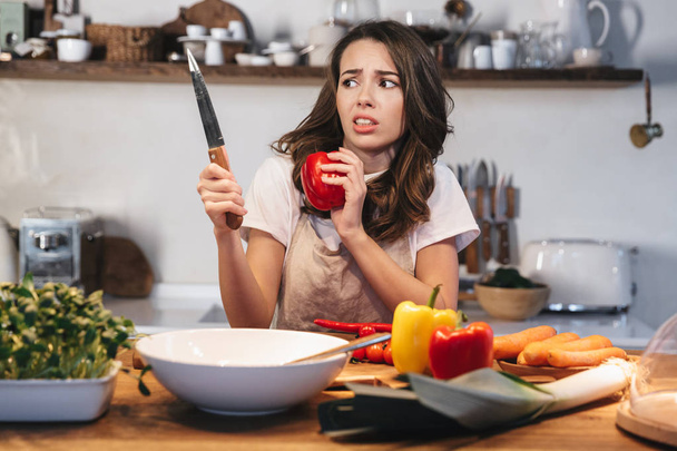 Beautiful young woman wearing apron cooking vegetables - Foto, Bild
