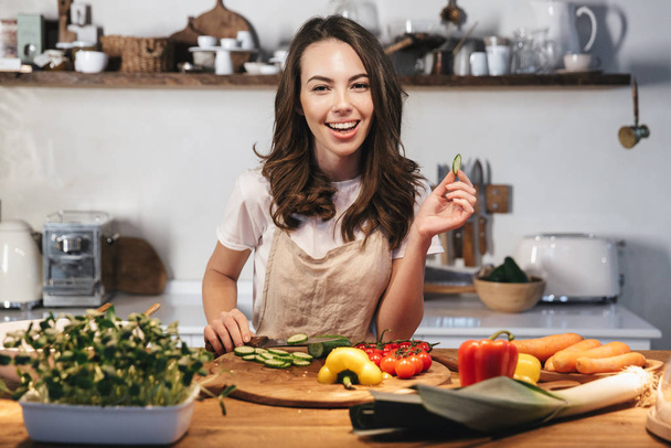 Beautiful young woman wearing apron cooking vegetables - Фото, зображення