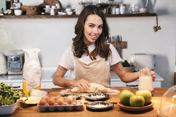 Cheerful young woman wearing apron preparing dough - Photo, image