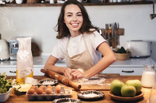 Cheerful young woman wearing apron preparing dough - Foto, Bild