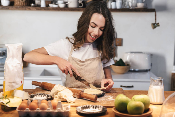 Cheerful young woman wearing apron preparing dough - Foto, Imagen