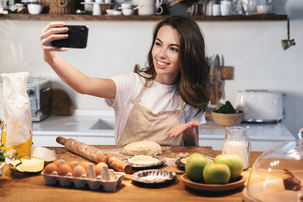 Cheerful young woman wearing apron preparing dough - Fotografie, Obrázek