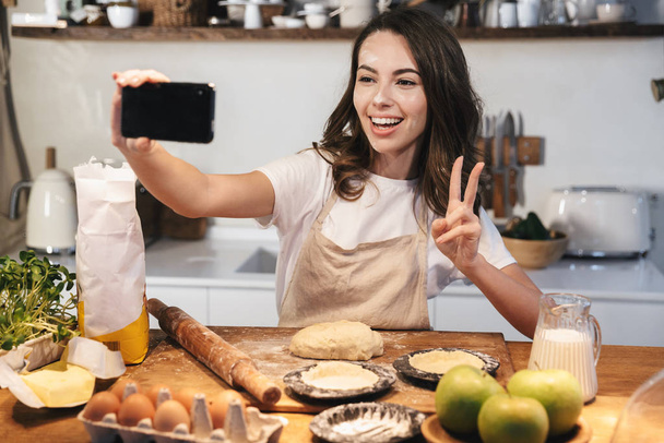 Cheerful young woman wearing apron preparing dough - Foto, imagen
