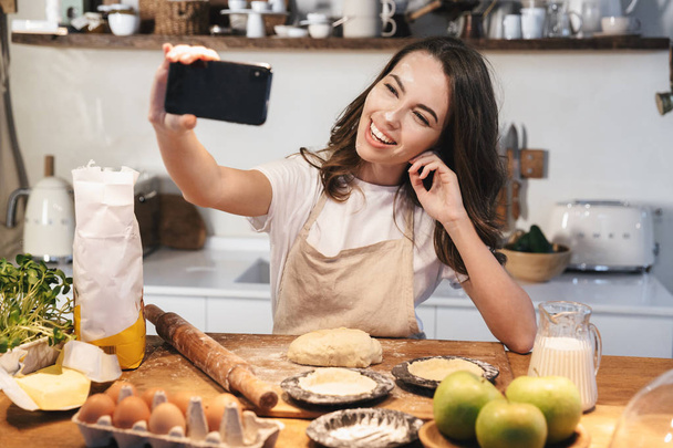 Cheerful young woman wearing apron preparing dough - Фото, изображение