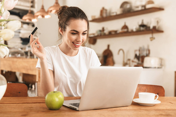 Belle jeune fille étudiante avec pomme à l'intérieur en utilisant un ordinateur portable tenant la carte de crédit
. - Photo, image