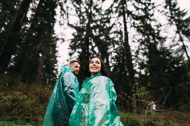 couple in love dressed in rubber raincoats climb up the mountain - Photo, Image