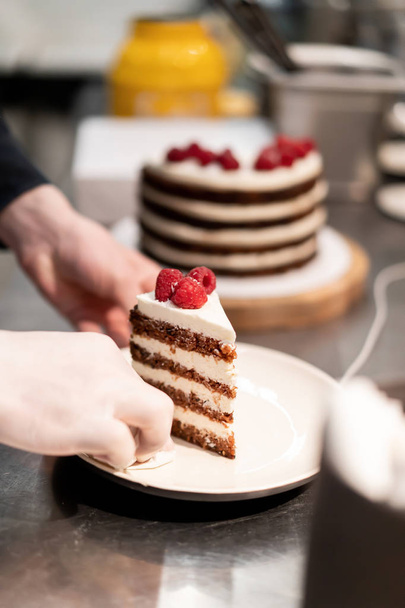 A man in a black shirt cuts with a knife a piece of sweet puff pie with red raspberry berries. Slice of dessert cake for a customer in a cafe. - Fotoğraf, Görsel