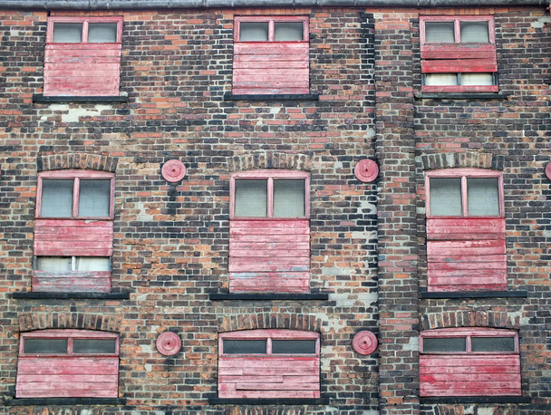 derelict old abandoned commercial building or factory with weathered brick walls and red painted boarded up windows - Photo, Image
