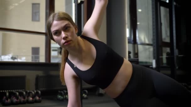 Circlind aroung view of concentrated sportsgirl standing in side plank with her phone lying nearby in gym. - Filmagem, Vídeo