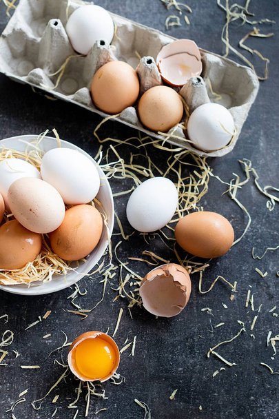 Νωπά οργανικά ωμά αυγά, λευκά, μπεζ και καφέ, το ένα είναι ραγισμένο - Φωτογραφία, εικόνα