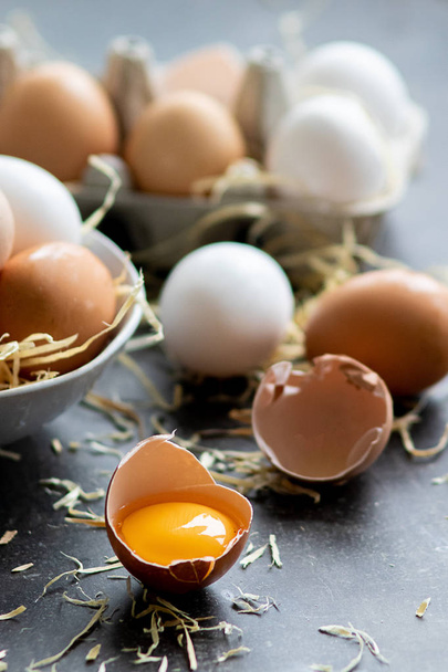 Verse biologische rauwe eieren, wit, beige en bruin, een is gebarsten - Foto, afbeelding
