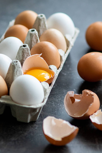Verse biologische rauwe eieren, wit, beige en bruin, een is gebarsten - Foto, afbeelding