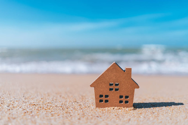 Pequeño modelo de casa en la playa de arena con fondo azul cielo
. - Foto, Imagen