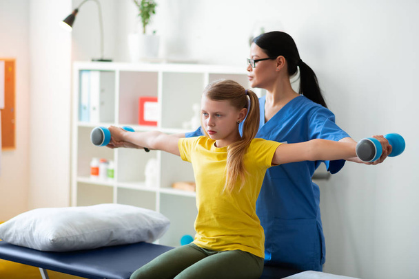 Diligent light-haired girl in yellow t-shirt repeating postures of active nurse - Photo, Image