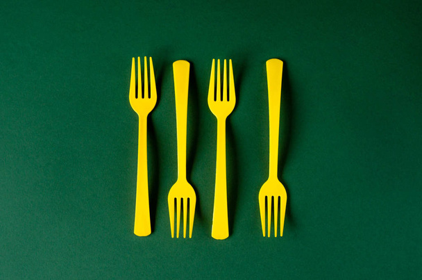 Plastic yellow forks on a green background. - Photo, Image