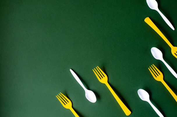 Tenedores de plástico amarillo y cucharas blancas sobre un fondo verde
.  - Foto, imagen