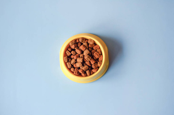 Ένα κίτρινο μπολ σε μπλε φόντο με τροφές για ζώα συντροφιάς. - Φωτογραφία, εικόνα