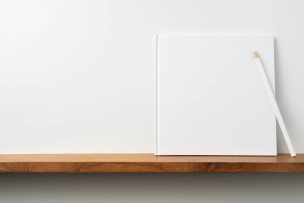 Square white notebook with pencil on bookshelf and white wall for mockup - Foto, immagini