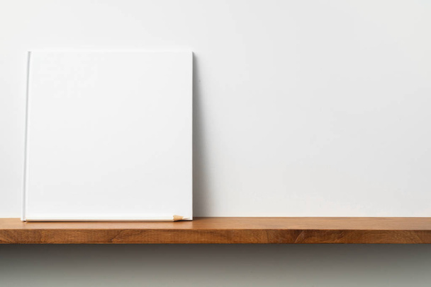 Square white notebook with pencil on bookshelf and white wall for mockup - Foto, afbeelding