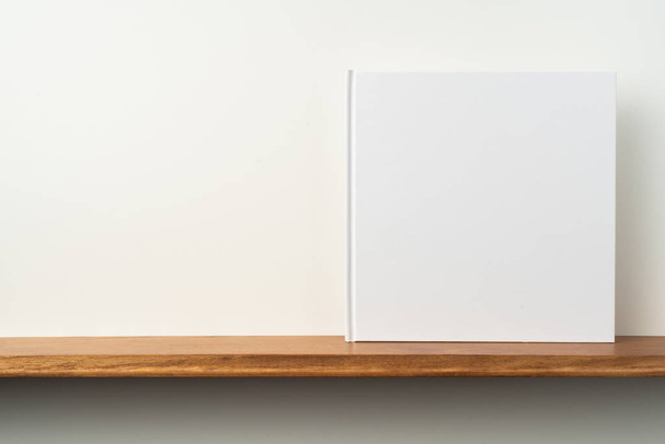 Square white notebook on bookshelf and white wall for mockup - Foto, Imagem