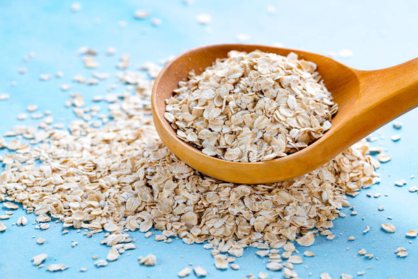 Dry oatmeal in wooden spoon on blue background. Oat flakes for healthy and dietary breakfast, slimming food - Φωτογραφία, εικόνα