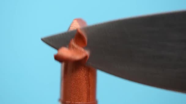 Metal sharp knife cuts brown lipstick into slices on a blue background. - Imágenes, Vídeo