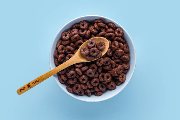 Cereals bowl and spoon with chocolate rings for dry breakfast on blue background. Top view  - Foto, Imagem