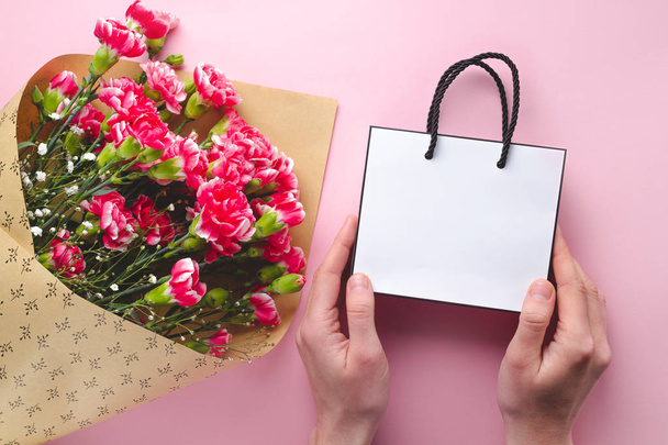 Bouquet of fresh carnations and a paper white gift bag on pink b - Foto, imagen