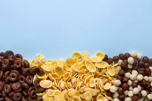 Mix of dry, chocolate balls, rings and yellow corn flakes for cereals breakfast on blue background. Copy space  - Φωτογραφία, εικόνα
