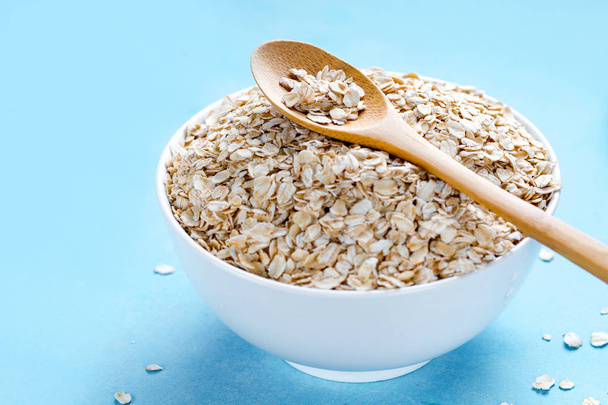 Dry oatmeal bowl with wooden spoon on blue background. Oat flake - Fotó, kép