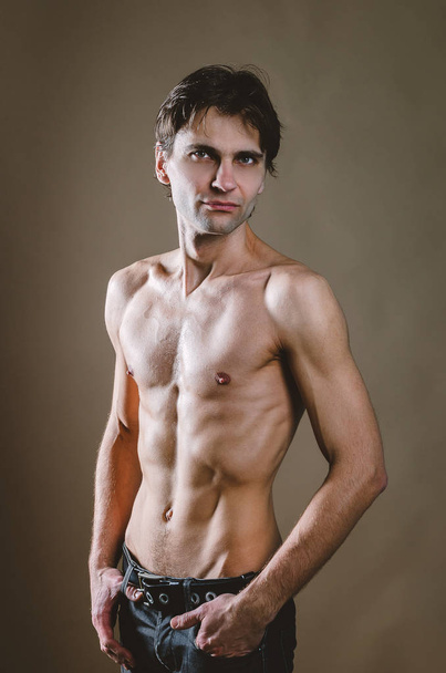 Naked torso of a young, slim, pumped-up man on a beige backgroun - Foto, afbeelding