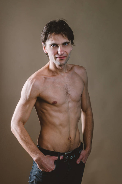 Naked torso of a young, slim, pumped-up man on a beige backgroun - Фото, зображення