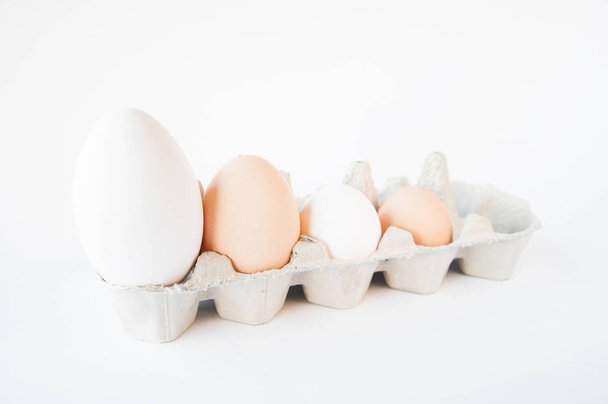 küçük bir tepside dört yumurta vardır. Büyükten küçe beyaz bir masada - Fotoğraf, Görsel
