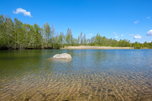 καθαρή διαφανή λίμνη νερού με πάτο άμμου και μεγάλο βράχο στη μέση. καλοκαιρινές πράσινες ακτές - Φωτογραφία, εικόνα